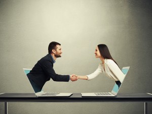 A couple shaking hands through a computer